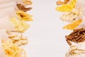 Golden colorful snacks - nachos, popcorn, croutons, chips in craft paper cone as border on white wood table.