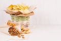 Golden colorful snacks - nachos, popcorn, croutons, chips in rustic basket and craft paper cone on white wood table.