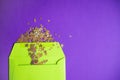Golden confetti pouring out of green envelope on purple background.