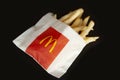 Golden crispy french fries wrapped in a paper bag from McDonald`s on black background. McDonald`s Corporation is an American fast