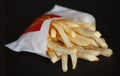 Golden crispy french fries wrapped in a paper bag from McDonald`s on black background. McDonald`s Corporation is an American fast