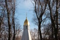 A golden cross on top of a white stone orthodox church and golden cupola surrounded by dark leafless branches of trees during a Royalty Free Stock Photo