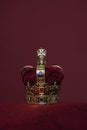 Golden crown on a velvet cushion on a deep red background with copy space in a vertical image Royalty Free Stock Photo