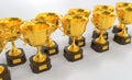 Golden cups, award trophy or winner prize on wooden pedestal, angle view. Rows gold goblets with bowls for championship
