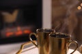 Golden cups with hot drinks against fireplace, closeup. Space for text Royalty Free Stock Photo