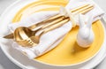 Golden cutlery in white napkin, white ceramic bunny on yellow white plates closeup. Easter table. Royalty Free Stock Photo