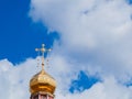 The Golden dome of an Orthodox temple on background of blue sky and clouds. Golden cross on the dome of the temple