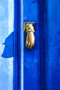 Golden doorknocker with hand shape on blue wooden door