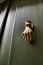 Golden doorknocker with hand shape on old green wooden door