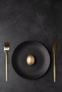 Golden egg on a black plate with a knife and fork Royalty Free Stock Photo