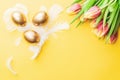 Golden eggs in basket with spring tulips, white feathers on pastel yellow background in Happy Easter decoration. Foil minimalist Royalty Free Stock Photo