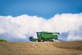 The golden field of ripe wheat under a blue sky with large white fluffy clouds. A green farm harvester reaps a ripened harvest