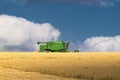 The golden field of ripe wheat under a blue sky with large white fluffy clouds. A green farm harvester reaps a ripened harvest Royalty Free Stock Photo