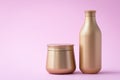Golden flacon of shampoo and a jar of mask. Cosmetic products on a pink background. Luxury beauty style, hair care concept. Clear