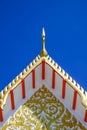 Golden gable apex on ornamental Thai temple roof against blue clear sky background