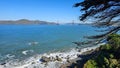 The Golden Gate Bridge at Mile Rock Beach with blue ocean water, waves, rocks and lush green trees on Lands End Trail Royalty Free Stock Photo