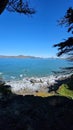 The Golden Gate Bridge at Mile Rock Beach with blue ocean water, waves, rocks and lush green trees on Lands End Trail Royalty Free Stock Photo