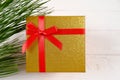 Golden gift box with red bow and ribbon, wooden background, pine branches, Christmas Royalty Free Stock Photo