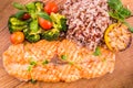 Golden grilled fish fillet with a side dish of rice and vegetables on a wooden board on a white background Royalty Free Stock Photo