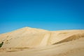 Golden hills of Giant sand dunes under cloudless blue sky. Tiny figures of people climbing up the dunes demonstrate the Royalty Free Stock Photo