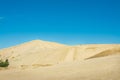 Golden hills of Giant sand dunes under cloudless blue sky. Tiny figures of people climbing up the dunes demonstrate the Royalty Free Stock Photo