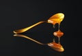 Golden honey dripping from a spoon on a reflective surface minimalist black background Royalty Free Stock Photo