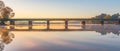 The golden hour casts a warm glow over a serene bridge, perfectly reflected in the still waters below as the sun sets on Royalty Free Stock Photo