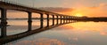 The golden hour casts a warm glow over a serene bridge, perfectly reflected in the still waters below as the sun sets on Royalty Free Stock Photo