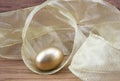 Gold egg investment nestled in golden ribbon on wood grain background