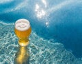 Glass of beer on the beach with crystal clear water and sun rays. Image created by artificial intelligence Royalty Free Stock Photo