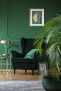 Golden lamp on elegant table next to dark green velvet armchair