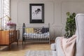 Golden lamp and heather in patterned pot on the vintage cabinet in grey baby room interior with crib and armchair Royalty Free Stock Photo