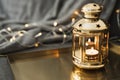 Golden lantern with burning candle standing on a metal tray, decorative lights as background