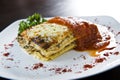 Golden lasagne with meat, tomatoes, cheese sauce and pasta in alternating layers on a wooden board garnished with basil