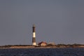 Golden light hitting the side of a lighthouse with dark stormy clouds overhead. Fire Island