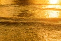 Golden light reflecting off a water wave at the sea and sand on sunset. Royalty Free Stock Photo
