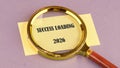 A golden magnifying glass is held over a yellow note that reads SUCCESS LOADING 2026. The note rests on a lavender surface Royalty Free Stock Photo