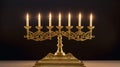 Golden menorah with seven gold candles lighting on dark background.