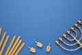 Golden menorah, yellow candles and Hanukkah dreidels with He, Pe, Gimel symbols on blue background, flat lay. Space for text Royalty Free Stock Photo