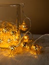 Golden metal balls garland in glass jar on light wooden table background. Christmas yellow gold garland lights from LED bulbs. New Royalty Free Stock Photo