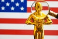 Hollywood Golden Oscar Academy award statue, magnifier and on american flag background with copy space. Success and victory conce