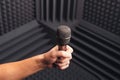 Golden microphone in hand, gray background with acoustic foam in studio