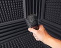 Golden microphone in hand, gray background with acoustic foam in studio