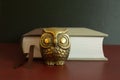 Golden figure of an owl in front of a book.