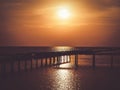 Golden natural sea sunset view of jetty or small bridge at horizon with silhouette and orange sky landscape. Sunset or sunrise