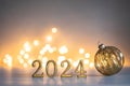 Golden 2024 new year numbers with a golden christmas ball on shiny background with soft atmospheric bokeh lights