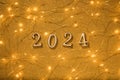 Golden numbers 2024 with Christmas lights on gold glitter texture background. 2024 new year coming