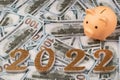 Golden numbers 2022 and a piggy bank against a background of one hundred dollar bills. Royalty Free Stock Photo