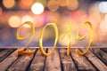 2019, golden numbers on wood table with blurred lights gold bokeh background