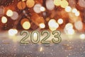 Golden numbers of year 2023. Glowing festive garland with bokeh on dark orange background.